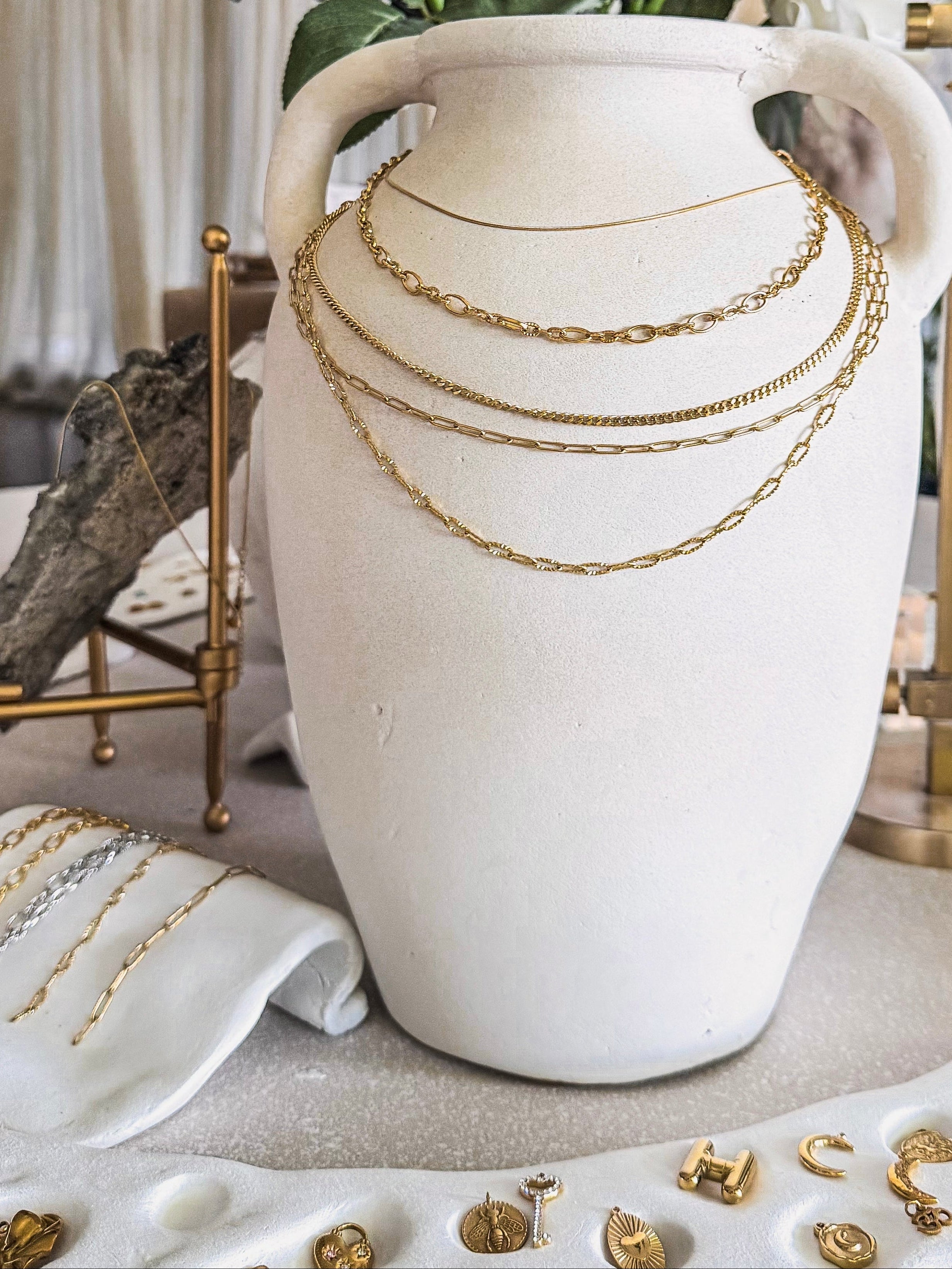 White vase with gold necklaces, surrounded by flowers and jewelry on a table.